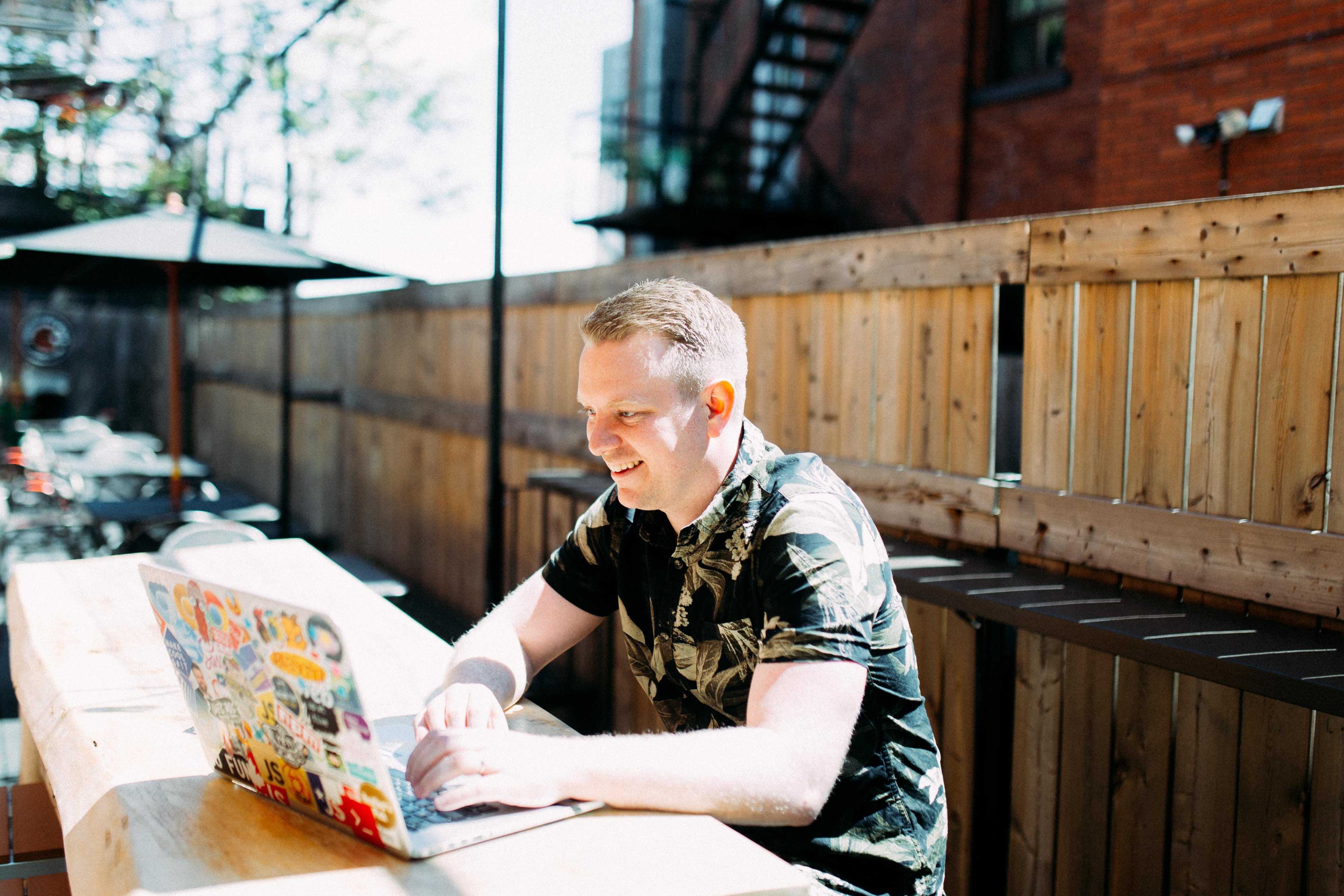 Wes Bos sits at a table in the direct sunlight pretending to be on his computer